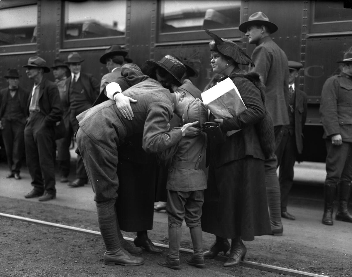 A soldier in uniform bids farewell to his wife and son.