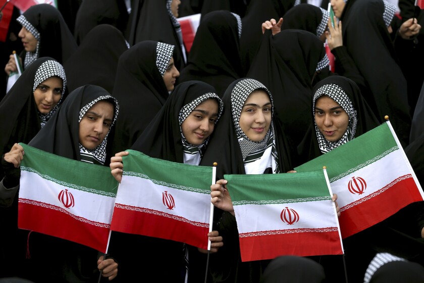 Young women hold national flags during an annual rally commemorating the anniversary of Iran's 1979 Islamic revolution