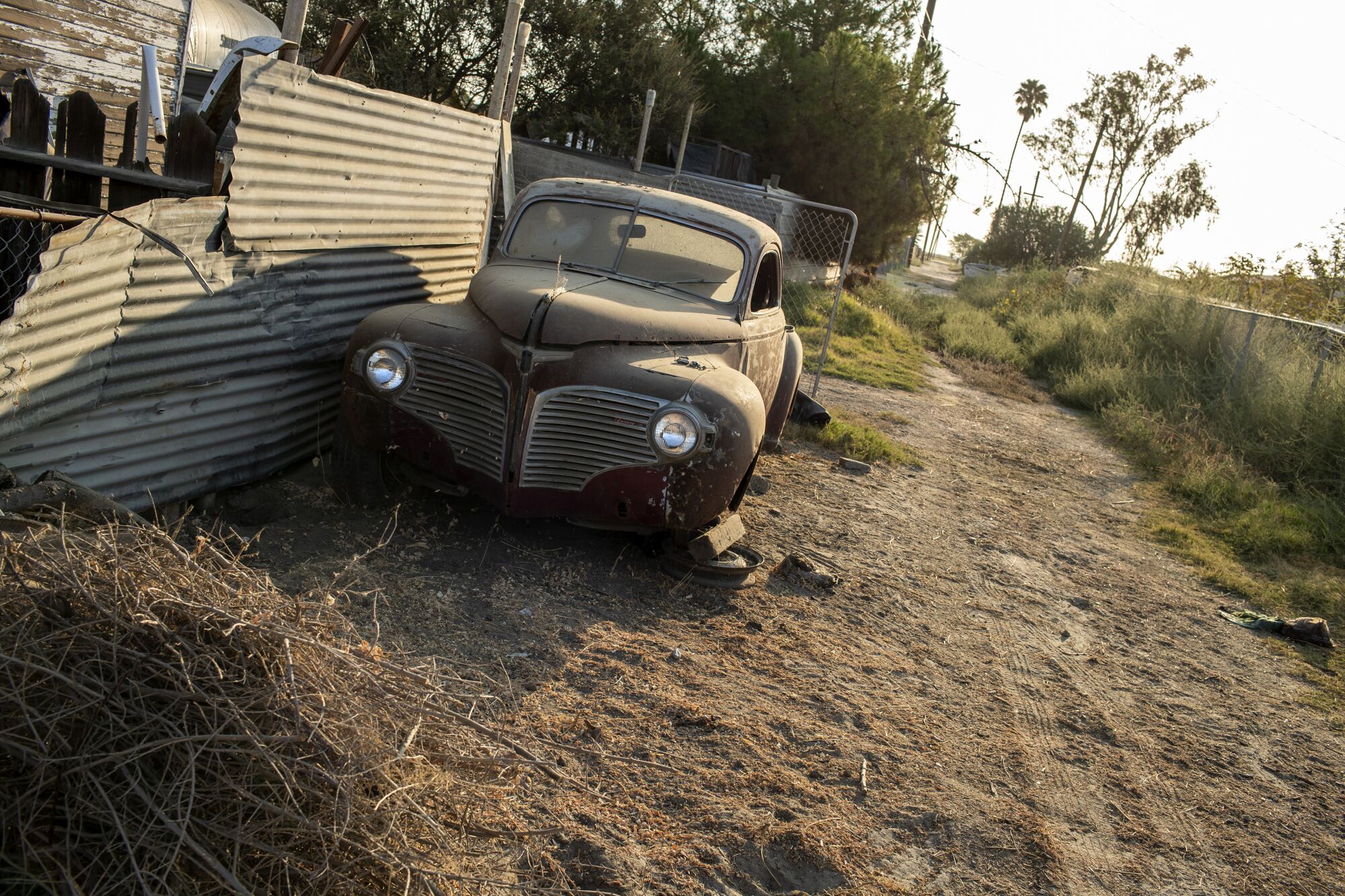 A vintage automobile sits on blocks in a dusty alley.