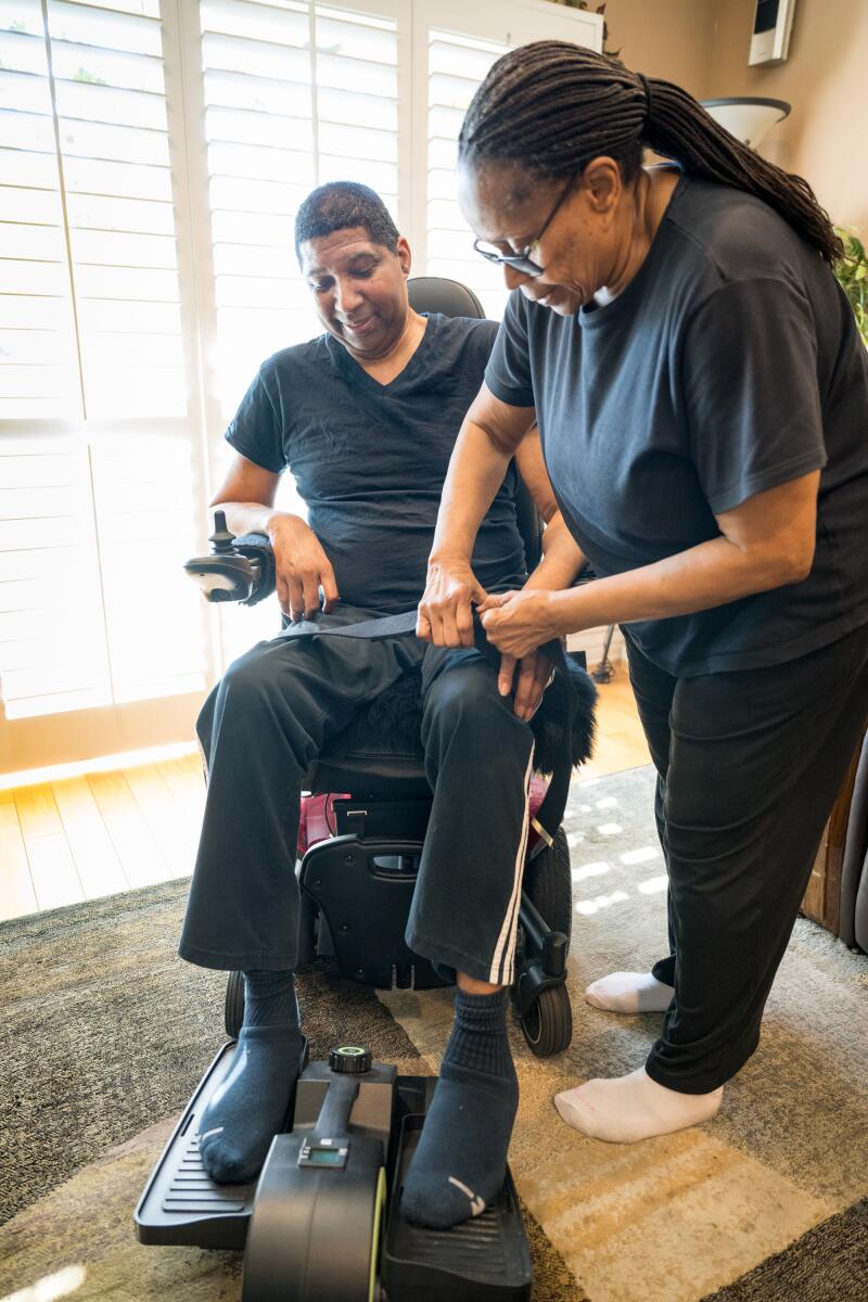 Rita Williamson straps together former UCLA star Rod Foster's legs so he can exercise his legs on a machine in his West L.A. home.