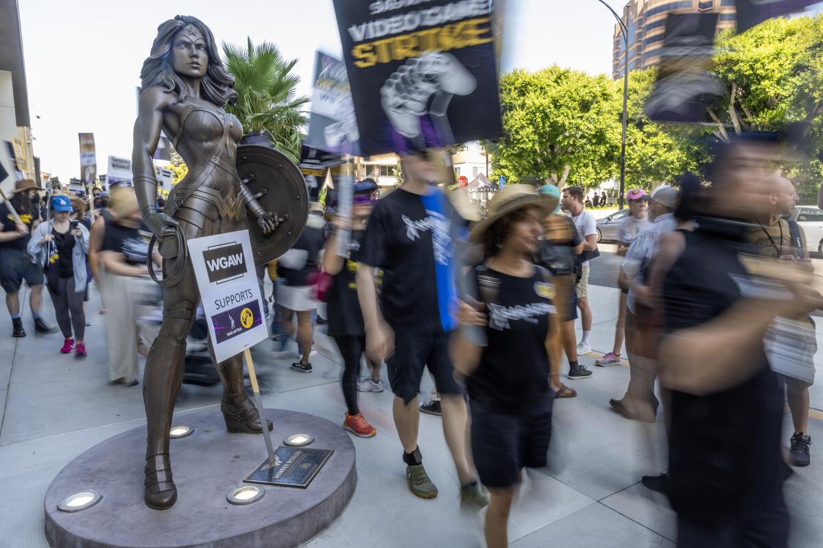 Picketers walk past a Wonder Woman statue at Warner Bros. Studio in Burbank.