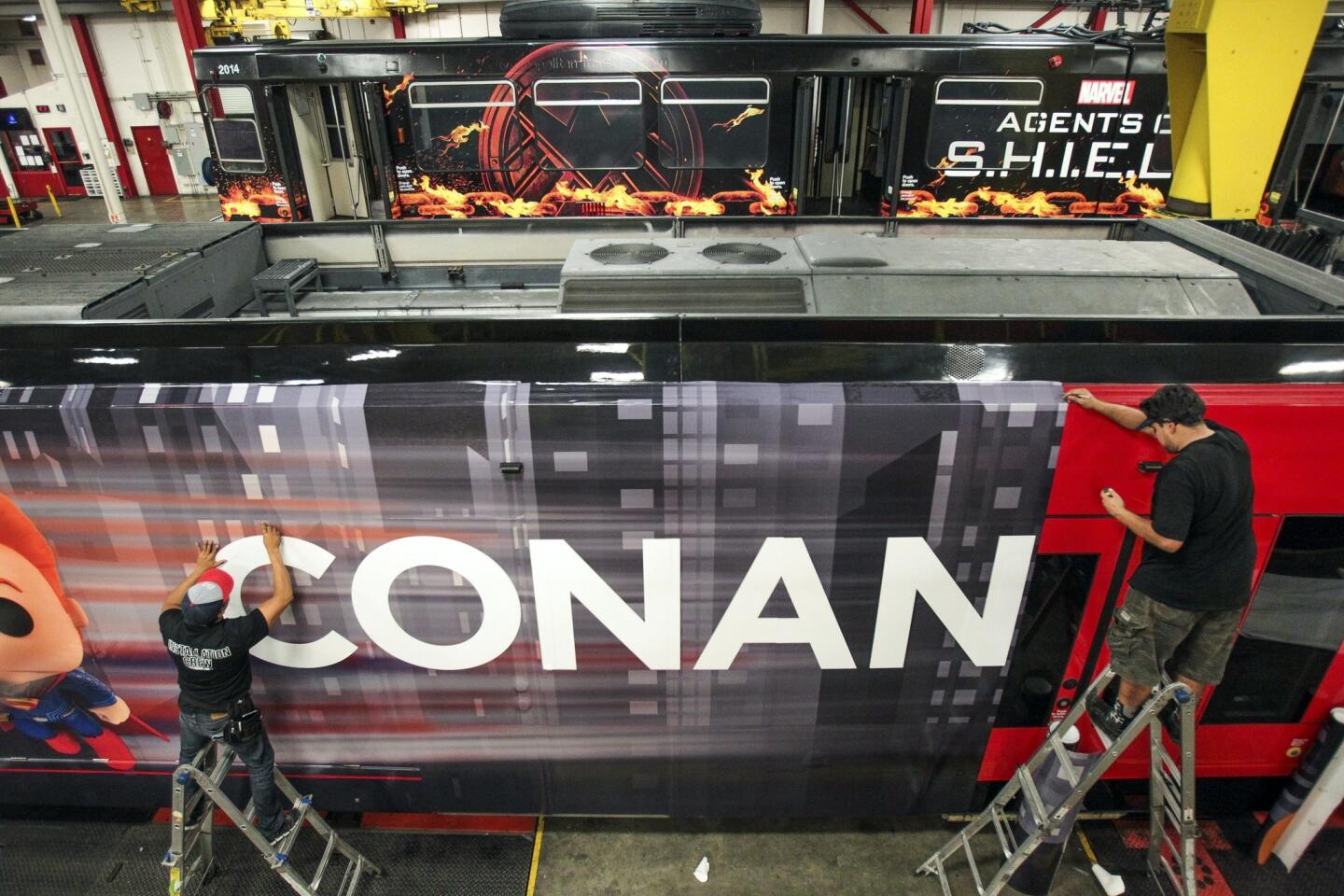 David Garcia, right, and Oscar Santos put on a section of transit vinyl as they and a crew put on an advertising wrap for TBS television host Conan O'Brien's talk show on a trolley car.