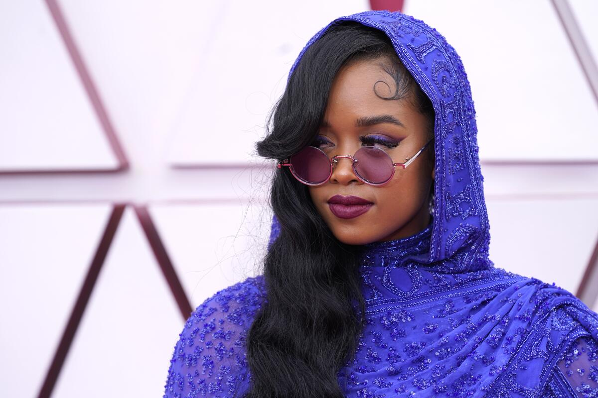 H.E.R. in a hooded purple outfit and round purple glasses