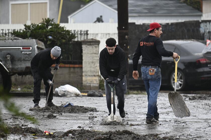 Residents clean debris from the street after flood waters inundated their neighborhood during a rain storm Monday, Jan. 22, 2024, in San Diego. (AP Photo/Denis Poroy)