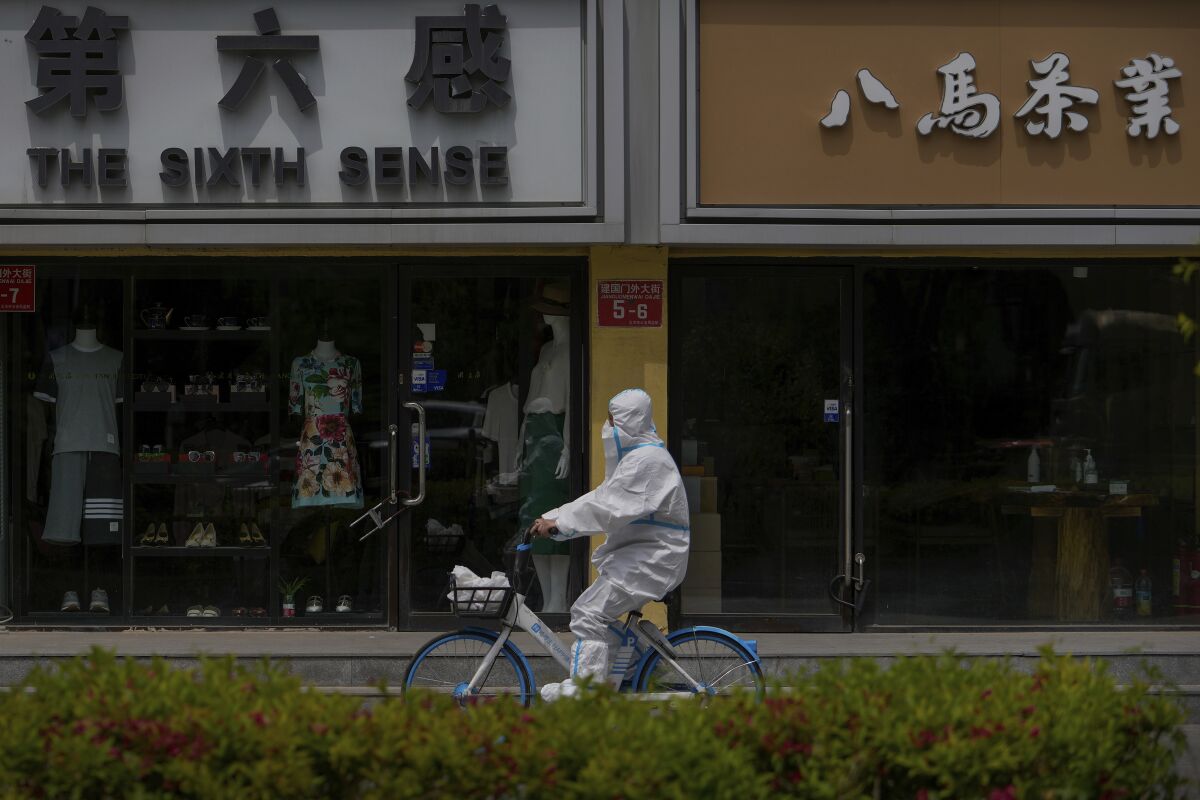 A worker in a protective suit rides a bicycle past shuttered retail shops after authorities ordered the closing down of non-essential businesses and asked people to work at home in the Chaoyang district on Monday, May 9, 2022, in Beijing. (AP Photo/Andy Wong)