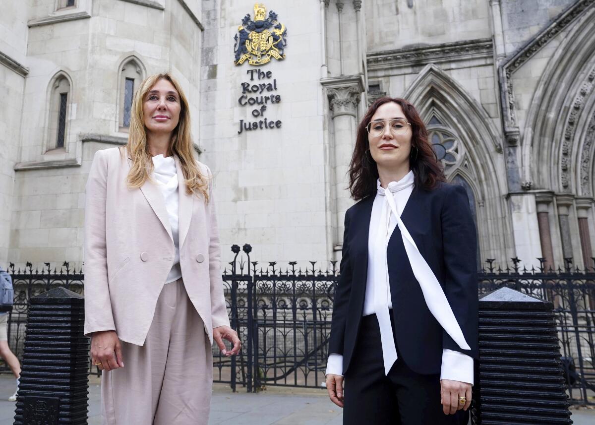 Two women stand in front of a historic building with gothic-arched windows and "The Royal Court of Justice" sign