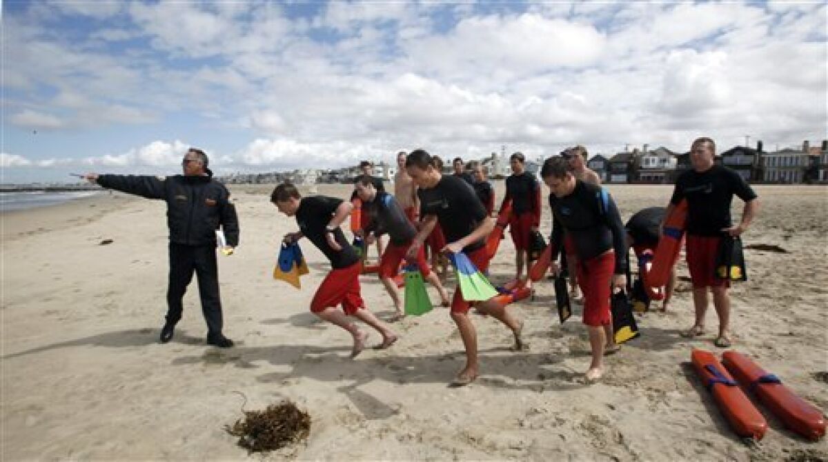 In this May 15, 2011 photo, lifeguard captain Arn Van Dyk, left, directs lifeguard trainees in a swimmer-rescue drill during a training session for new seasonal lifeguards at Newport Beach, Calif. Newport Beach’s 13-member, full-time lifeguard crew has gotten skeptical reactions ever since the local newspaper editorialized about lifeguard salaries, benefits and overtime pay that in at least two instances top $200,000 as the city struggles to rein in pension costs. (AP Photo/Reed Saxon)