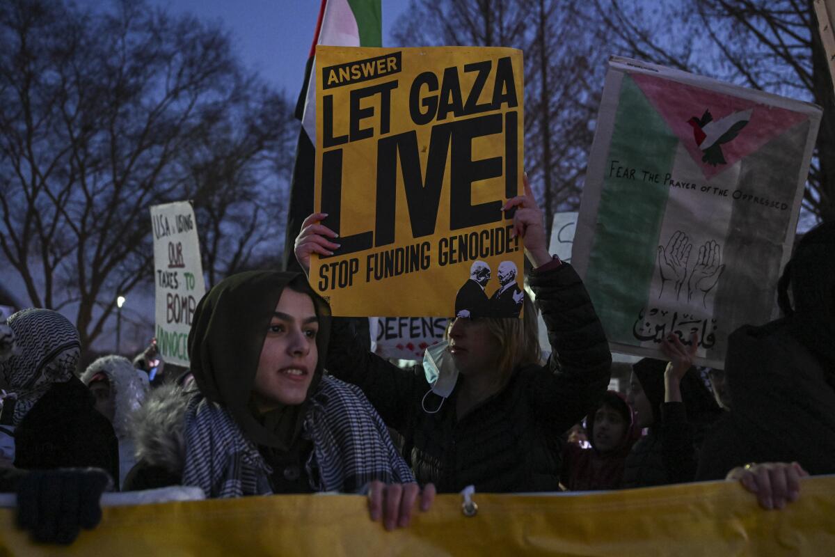 Protesters, including one with a sign that reads "Let Gaza live! Stop funding genocide."