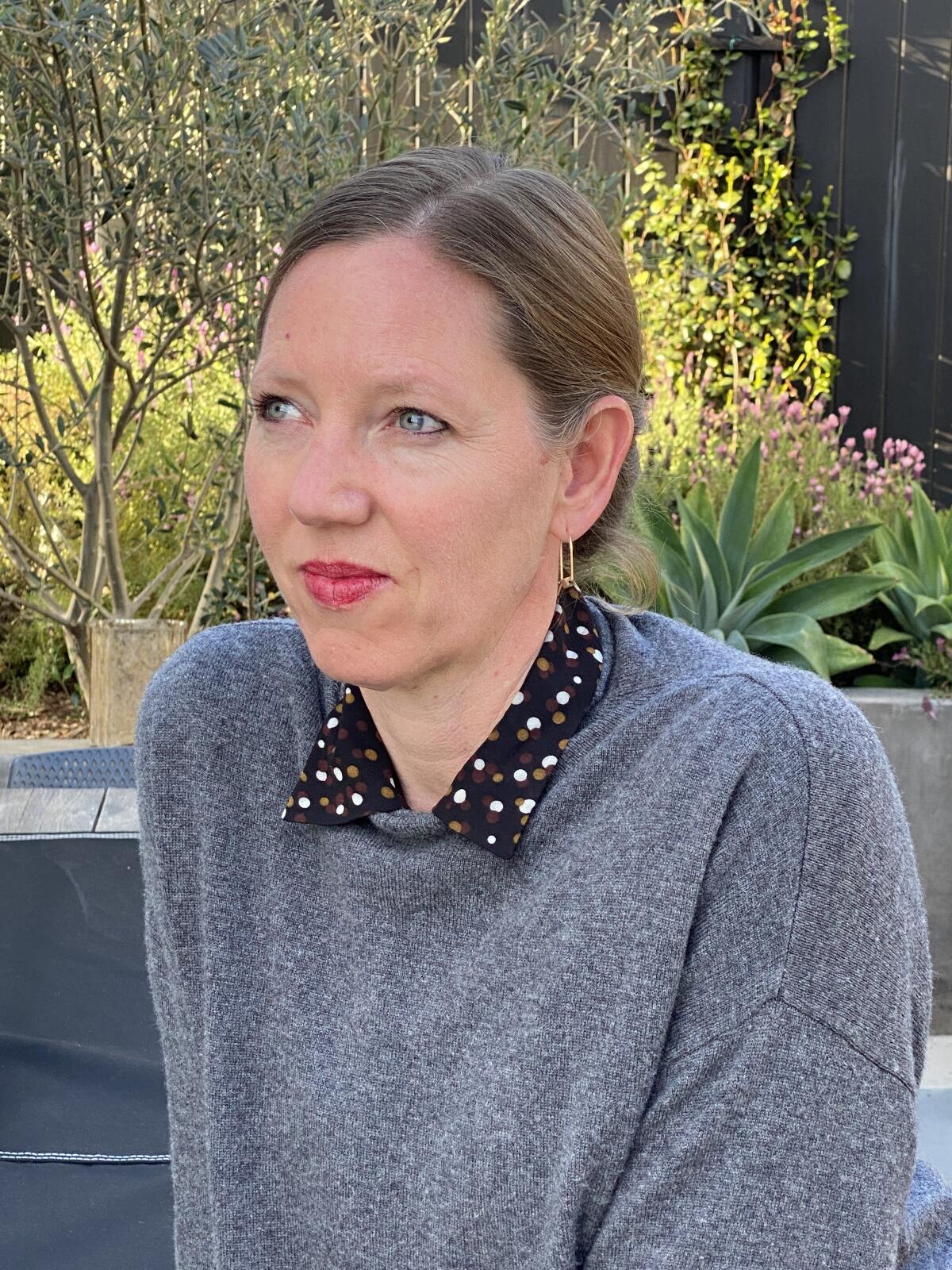 A woman in a gray sweater over a collared shirt looks to her right