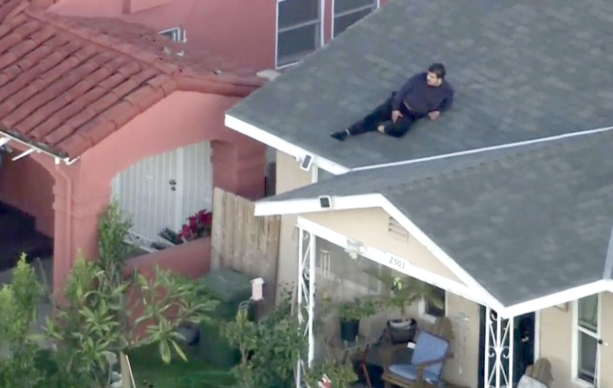 A man sits on a roof of a house, seen from above 