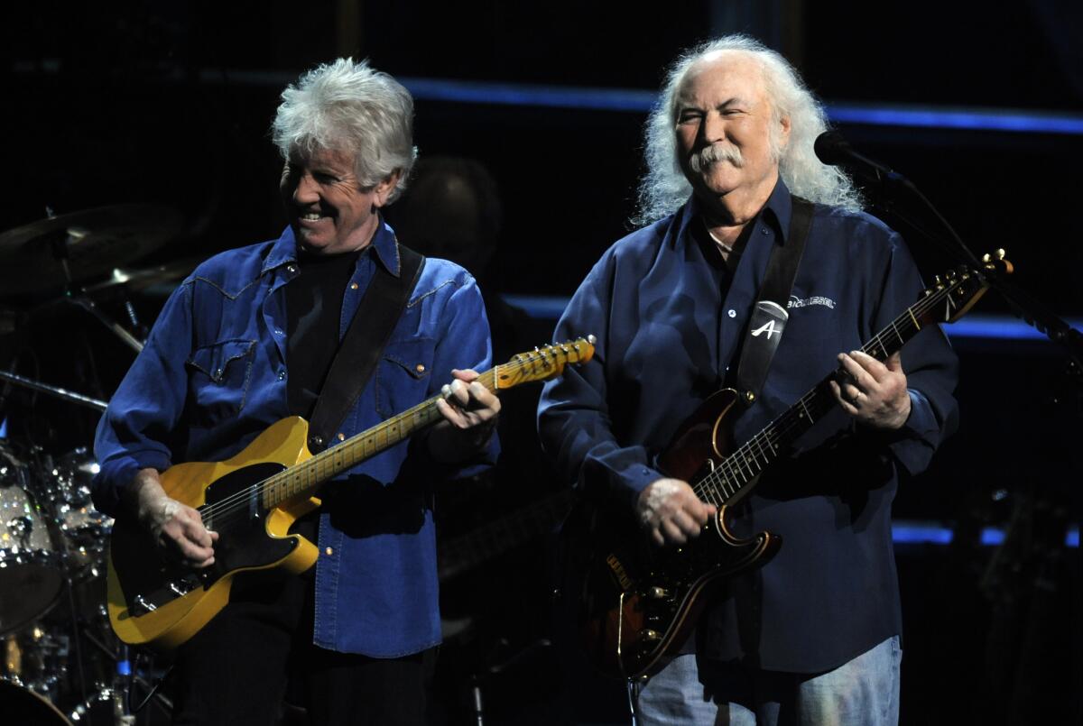 Two men with gray hair play electric guitars on stage.