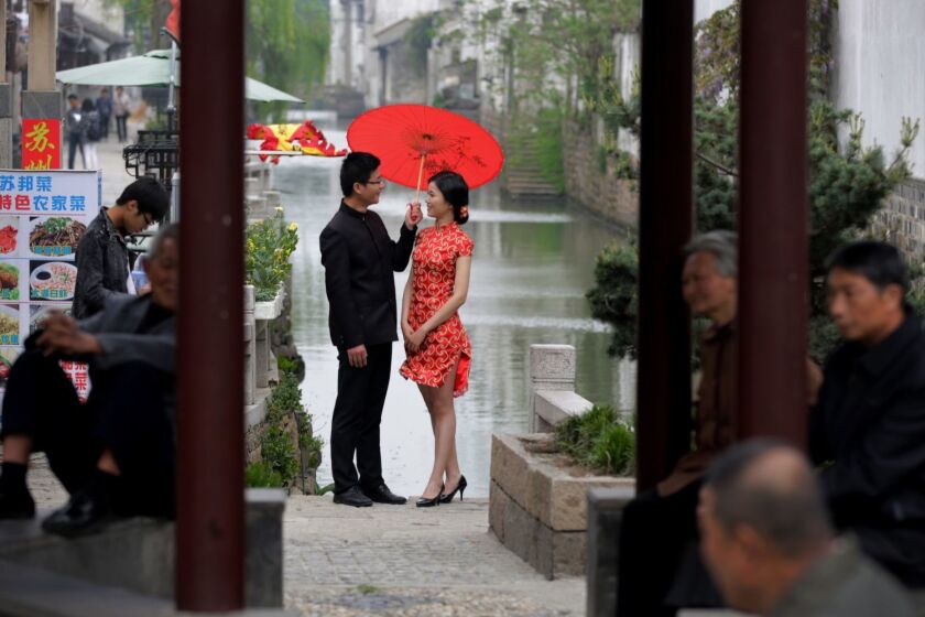 Residents take rest at a pavilion as a bride and groom, dressed a traditional costume, pose for wedding photos near Pingjiang steet in Suzhou in east China's Jiangsu province, Thursday, April 16, 2015. Pingjiang street was built along a canal and existed as early as the Song Dynasty, and is one of the famous tourist attractions in the country. (AP Photo/Andy Wong)