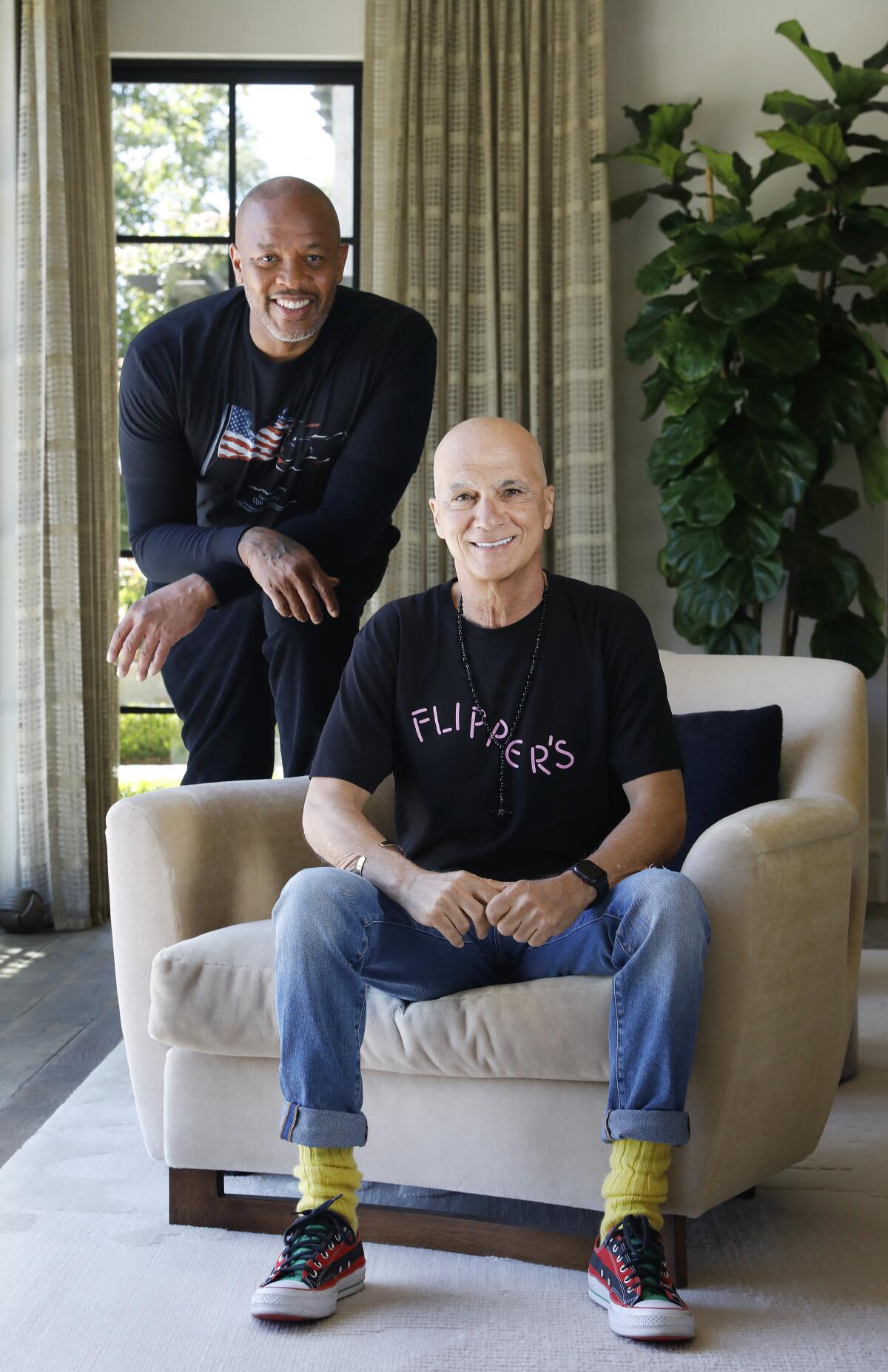 Dr. Dre and Jimmy Iovine pose in a sunny seating area. 