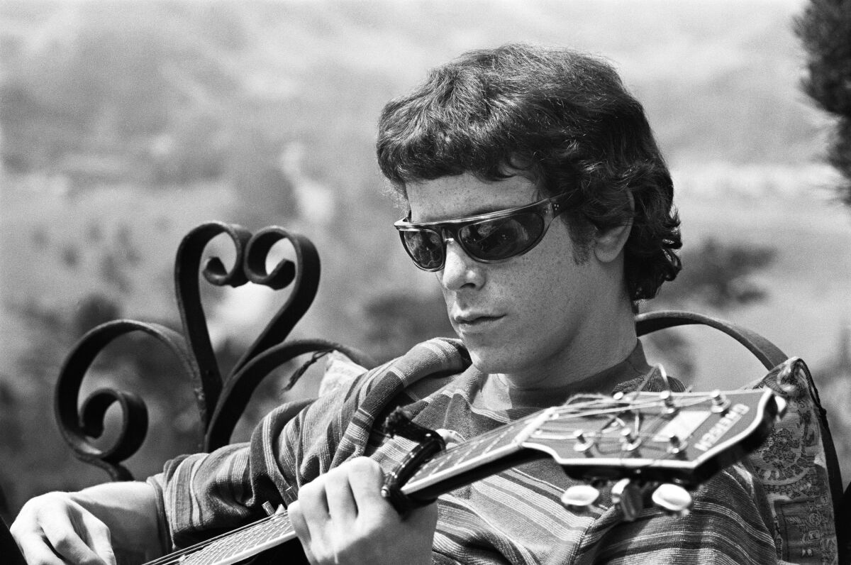 Lou Reed in sunglasses and holding a guitar.