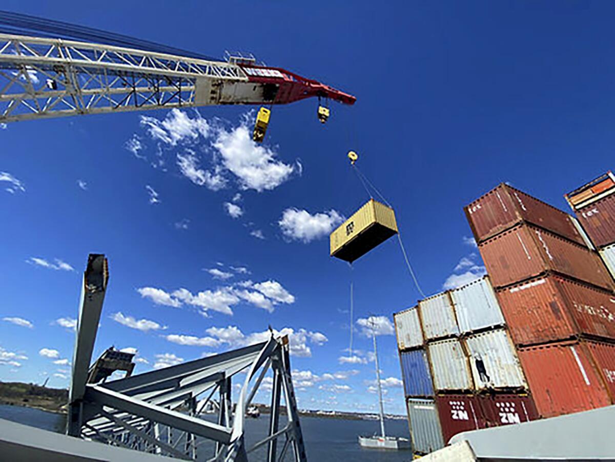 Crews remove shipping containers from the cargo ship Dali using a floating crane barge.