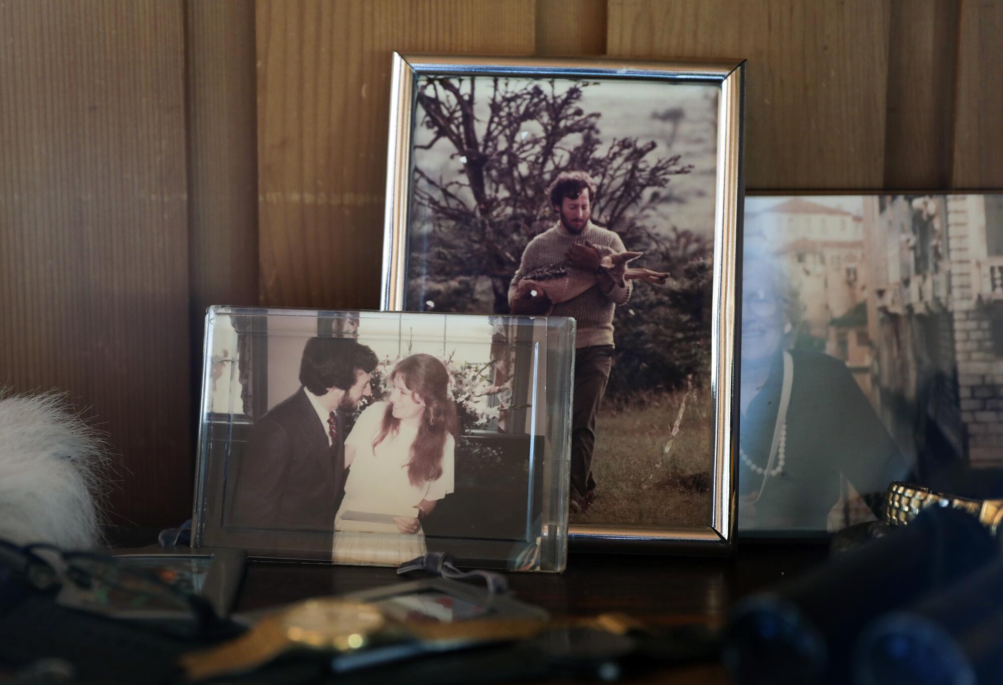 Framed family photos crowd a table in front of wood paneling. 