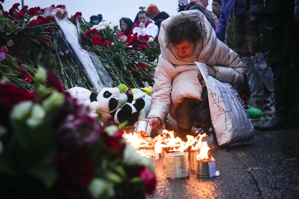 A woman lights candles near lines of roses placed against a fence.