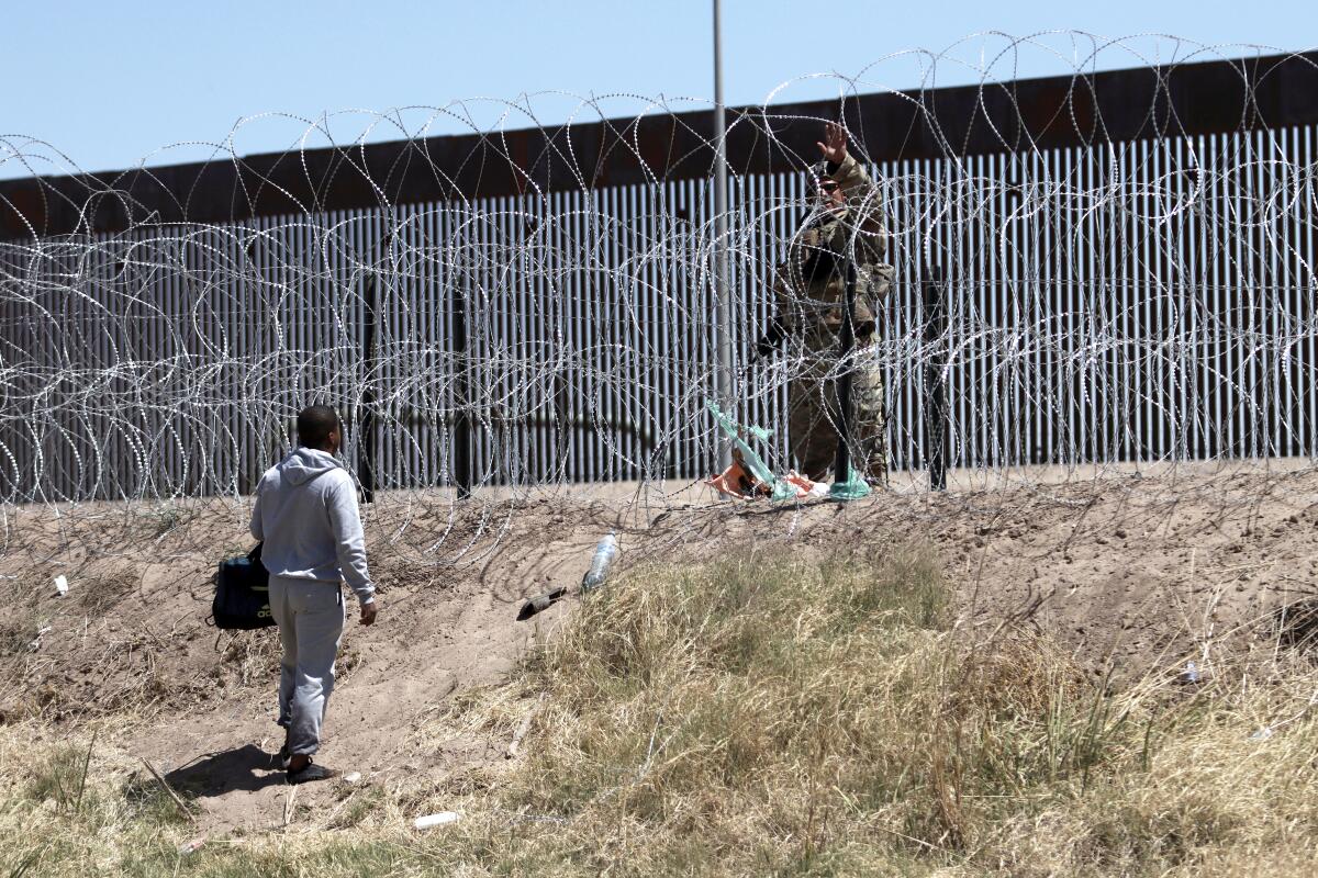 A migrant talks with a U.S. member of the armed forces, who is standing behind a barbed-wire fence.