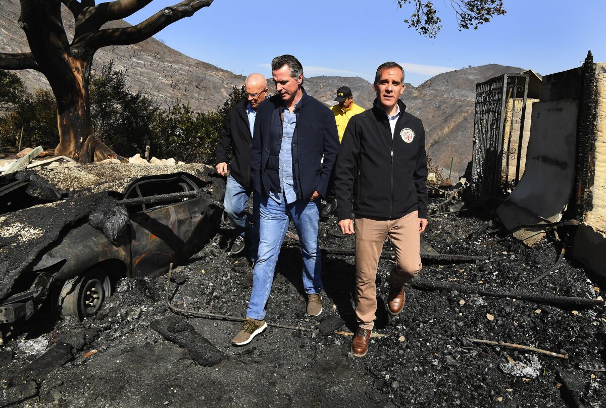 Gavin Newsom and Eric Garcetti lead a group walking past a burned tree and vehicle.
