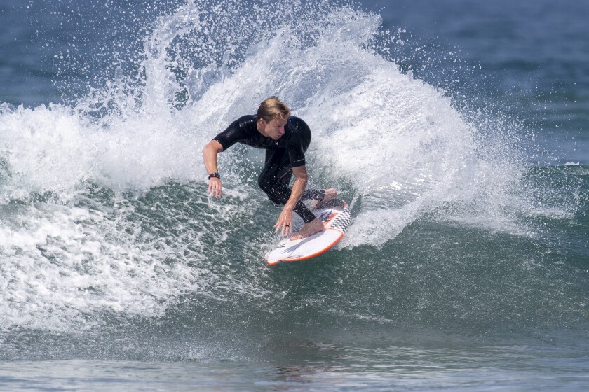 Huntington Beach, CA - July 13: USA Surfing Team member Kolohe Andino, 27, of San Clemente, does a slashing turn on a small wave as Brett Simpson, of Huntington Beach, (not pictured) a two-time U.S. Open winner and inaugural USA Surf Team head coach and Dino Andino, former pro surfer and Kolohe's father, (not pictured) watch while getting in some last minute training at Bolsa Chica State Beach in Huntington Beach before he heads to the Tokyo Summer Olympic Games Tuesday, July 13, 2021. Surfing will make its Olympic debut where it will be on display for the first time. Simpson coached Andino and offered advice on surfboard choices that would work well in Japan. It was Andino's last practice before heading to Japan on Wednesday. Andino turned heads in the water and on the beach as surfers were surprised to see the well-known local Olympian among them at a surf spot not known for high-performance perfect waves. Andino took time to pose for a photo with a young surfer on the beach after his training session. Andino will be joining John John Florence, of Hawaii, representing U.S.A. Another fellow San Clemente surfer, Caroline Marks will be joining Carissa Moore of Hawaii as they represent the U.S.A. women's team. (Allen J. Schaben / Los Angeles Times)