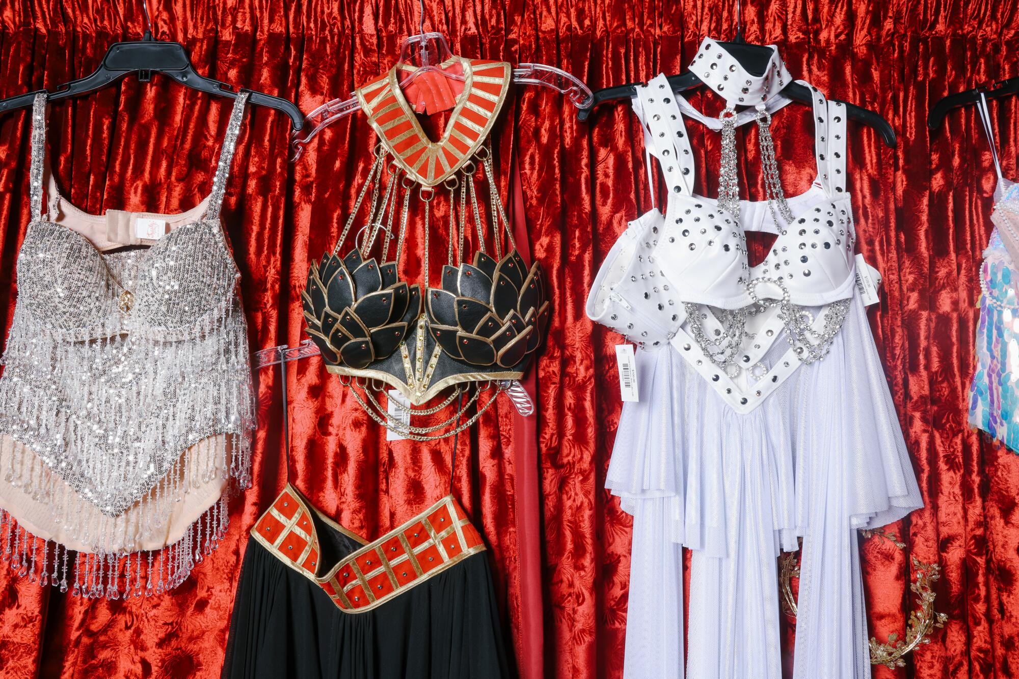 Three costumes from Trashy Lingerie hang on a wall against a red velvet curtain.