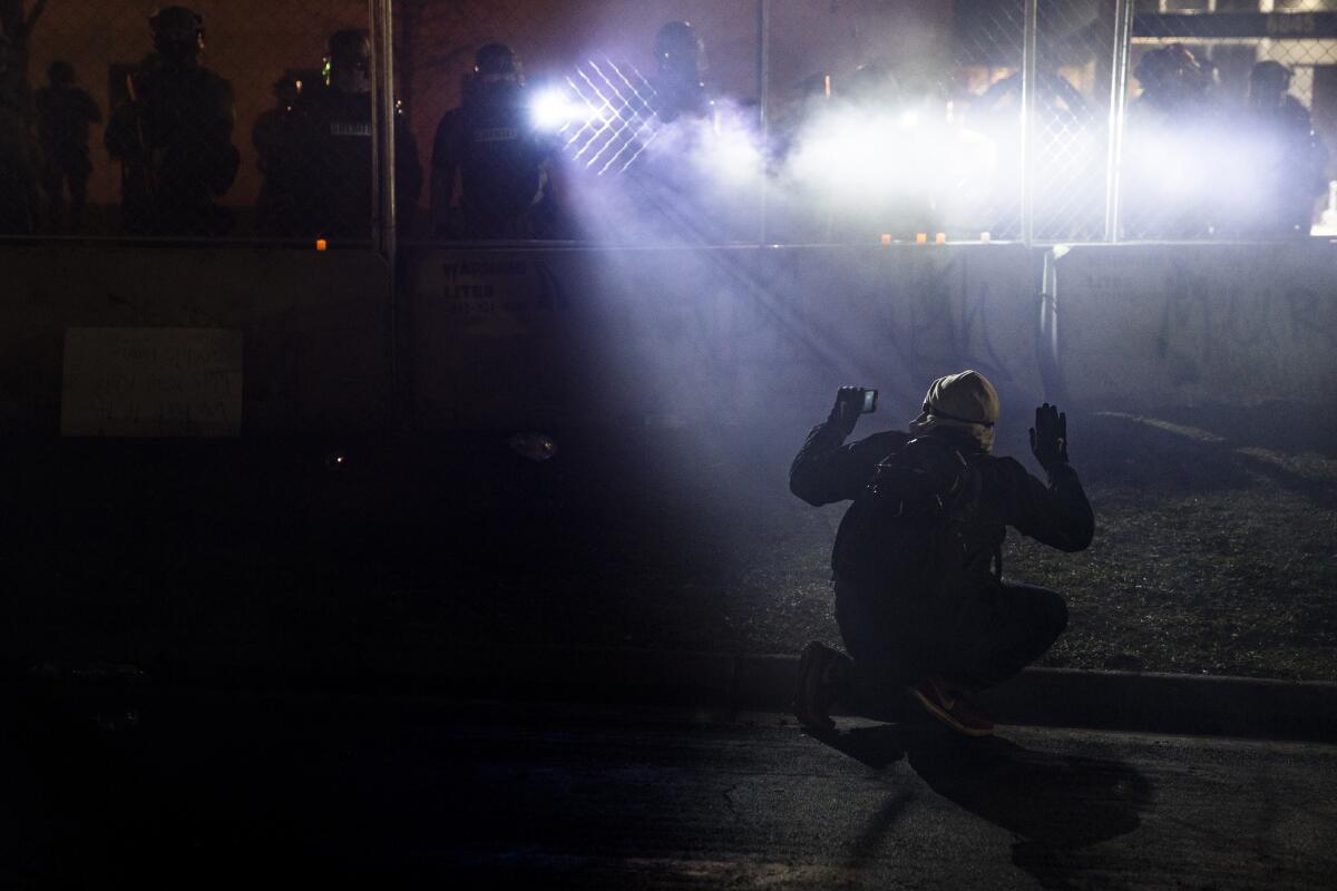 Police shine lights on a demonstrator with raised hands during a protest. 