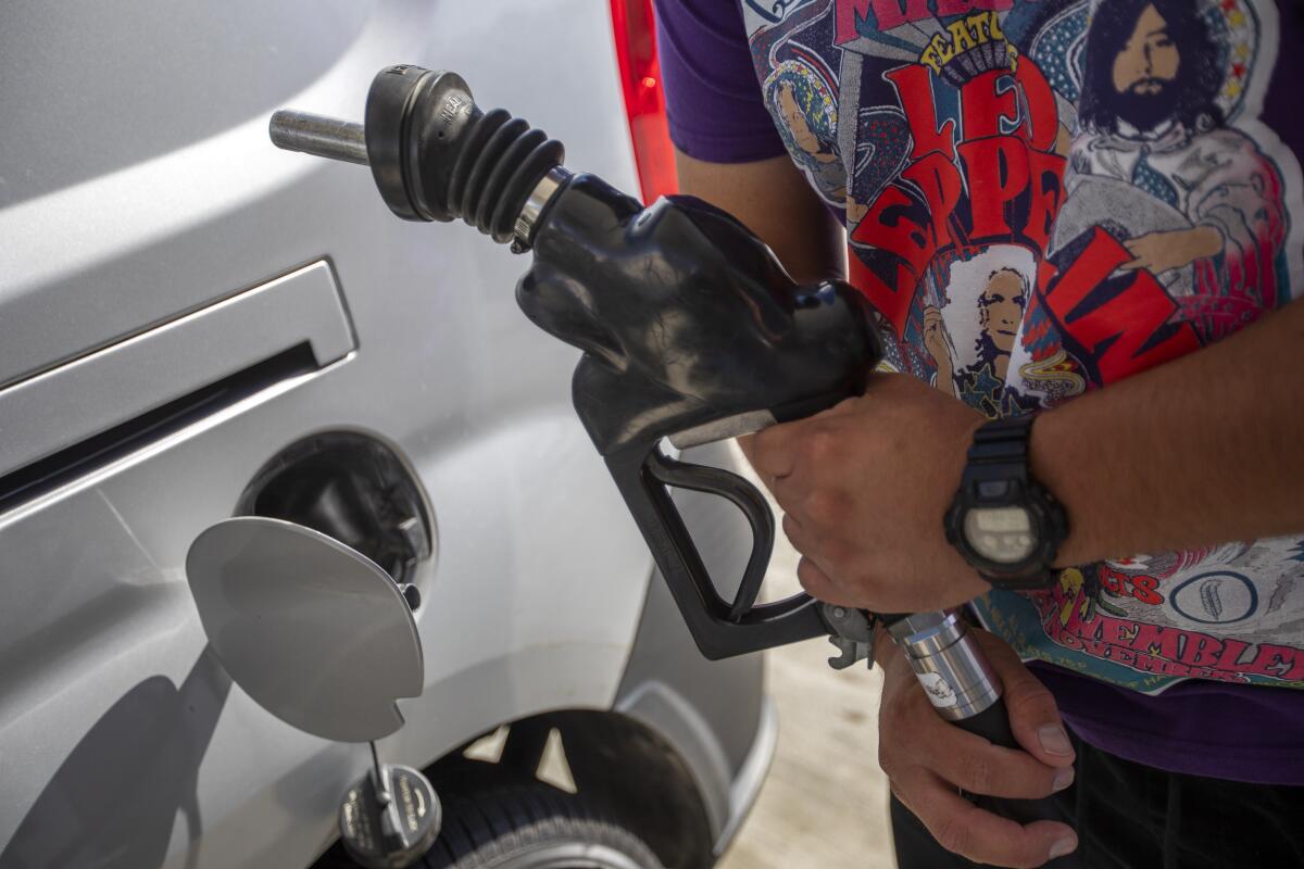 A man holds a gas pump in his hands beside his open gas tank with the cap dangling