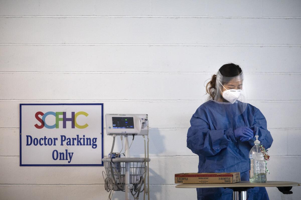 A doctor cleans her gloved hands with hand sanitizer in a makeshift parking lot facility