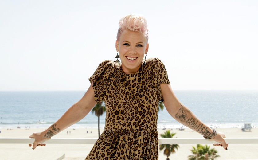 Pink leans against a railing with the ocean behind her