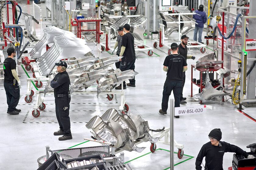 Scenes at the Tesla car factory include workers organizing parts for assembly.