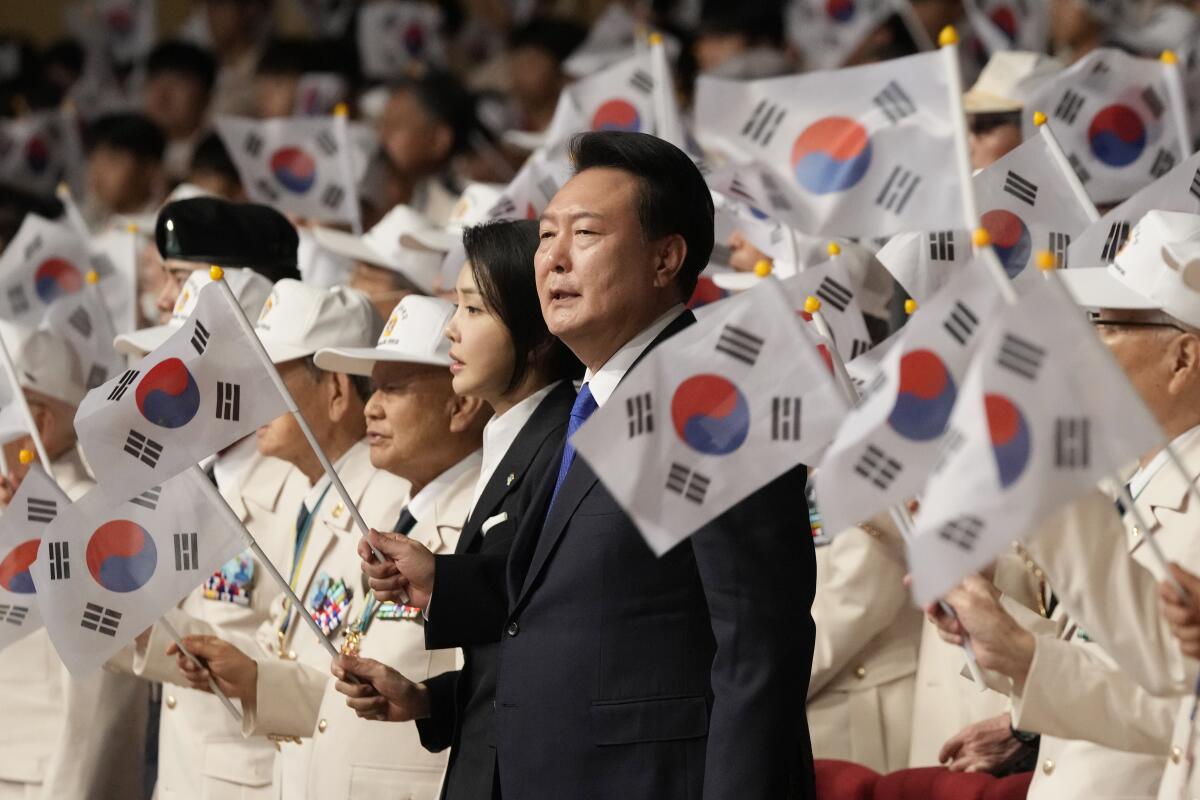 A woman and a man stand among people holding small flags.