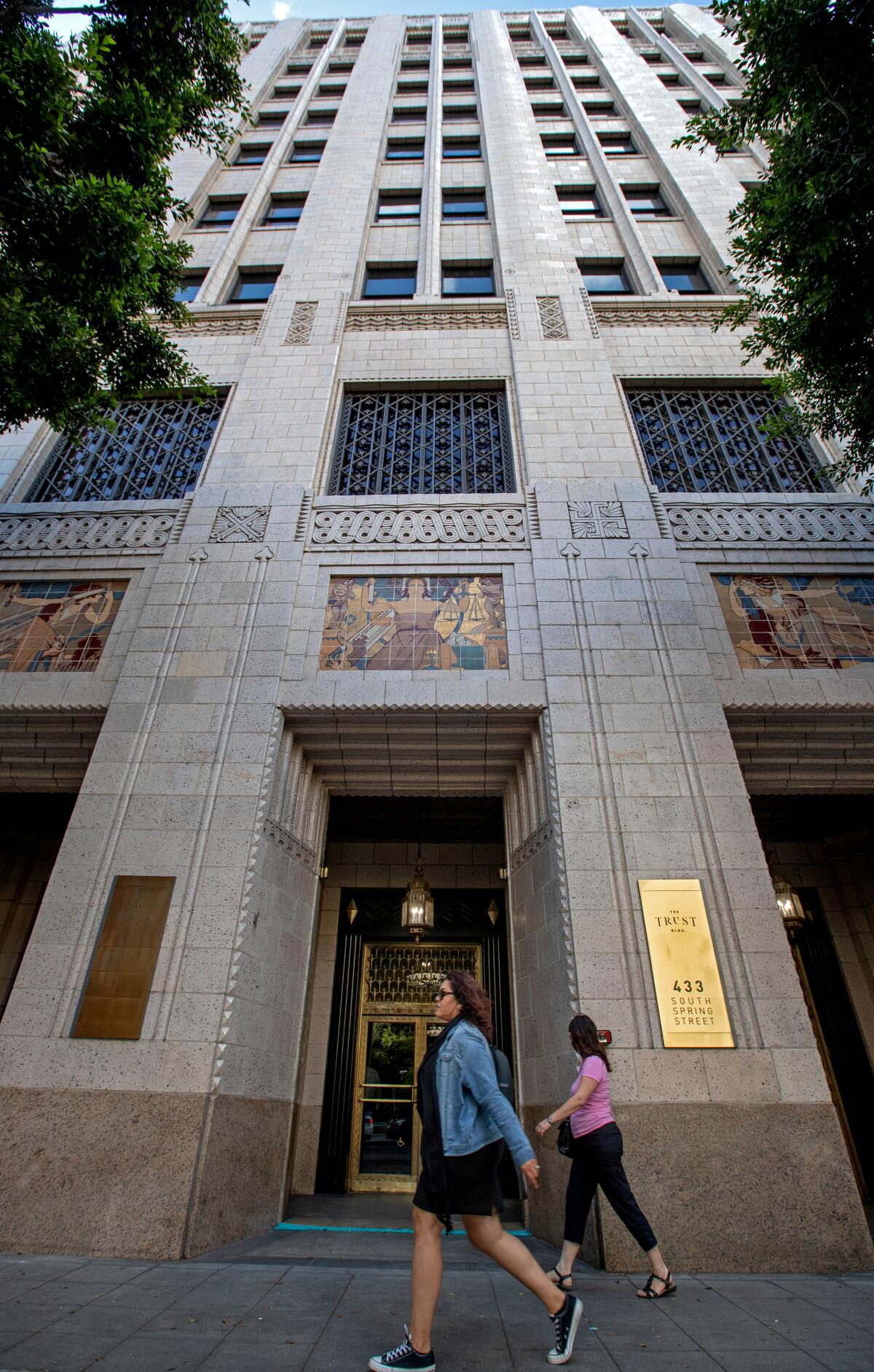 A vertical exterior of the Trust Building as two women walk in the foreground.