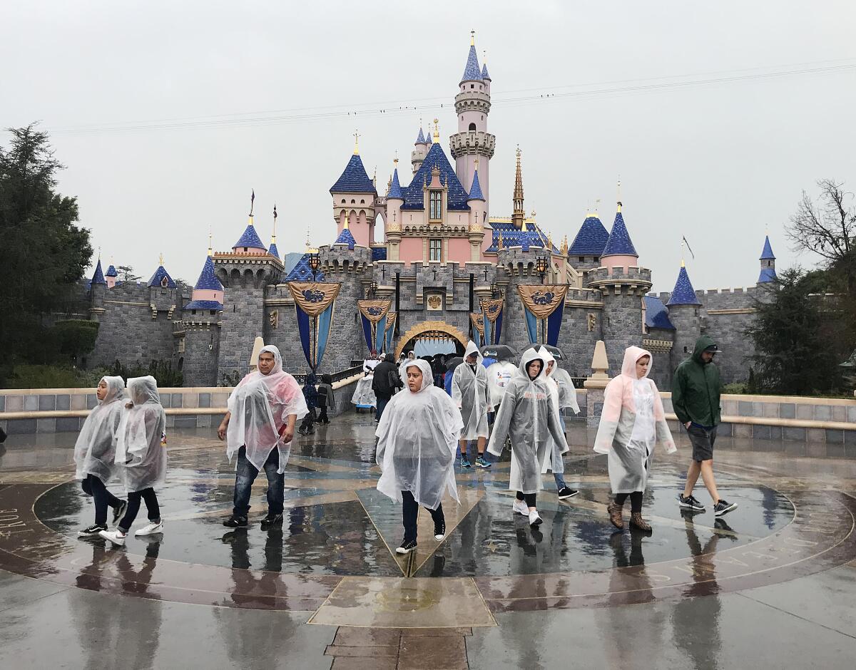 A group of people in rain ponchos walking in front of Sleeping Beauty Castle at Disneyland