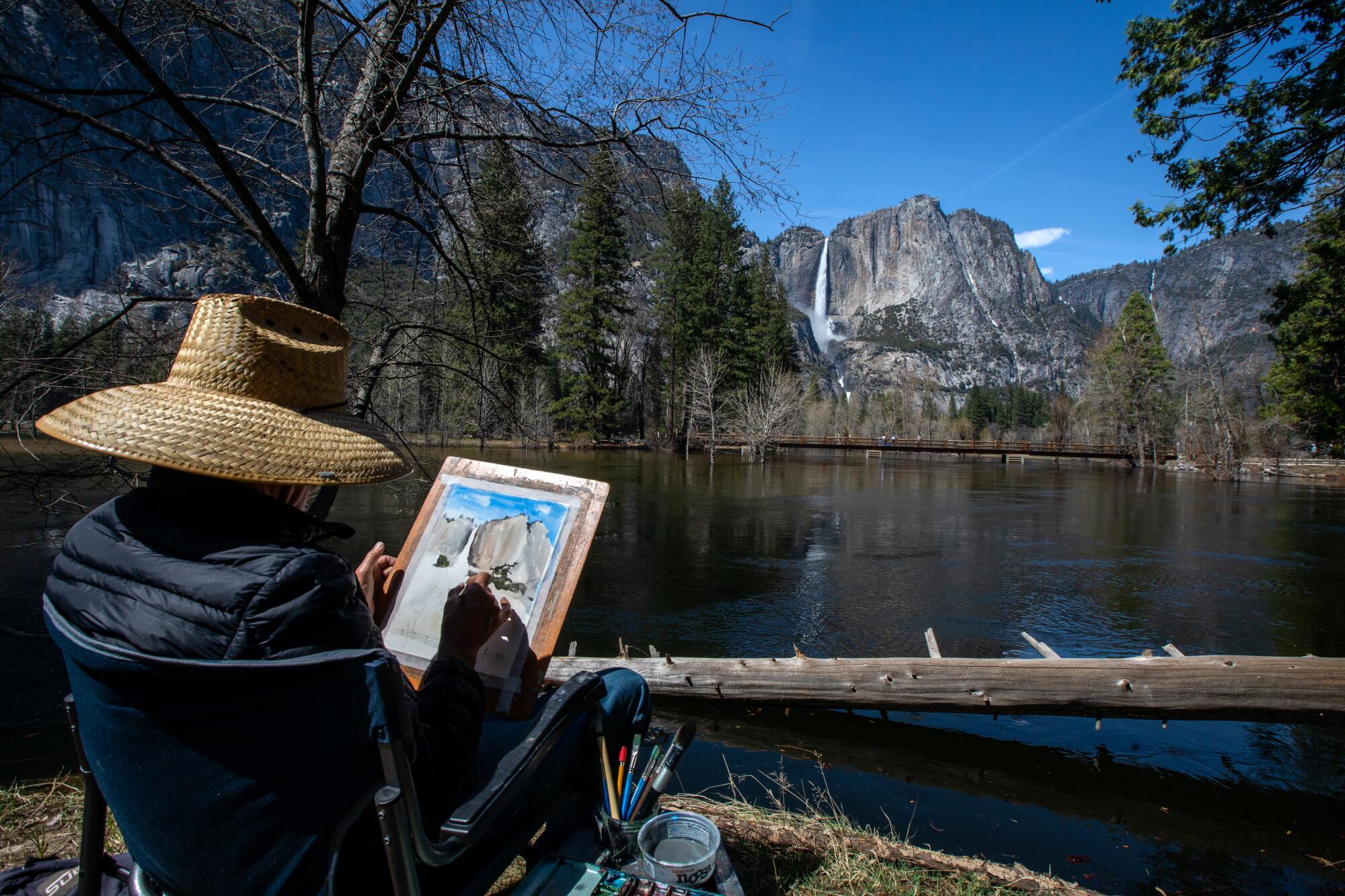 A man in a hat paints a Yosemite Valley scene.