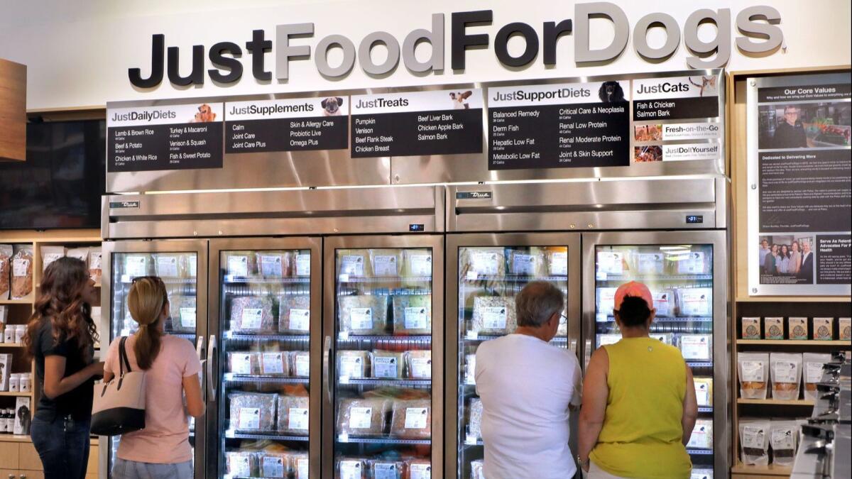 Customers at the PetCoach store examine the selection of Just Food For Dogs in a frozen food display case.