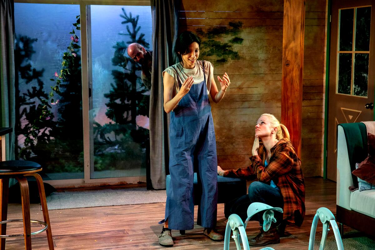 Two women talk inside their home while a man peers in through the sliding glass door.