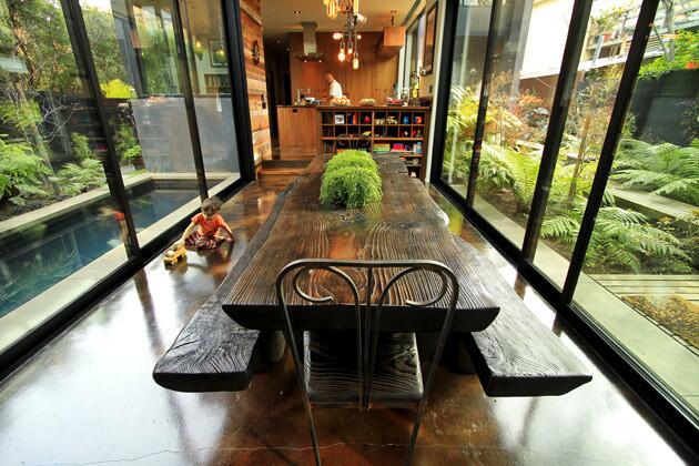 The dining room, looking toward the kitchen. The dining room table is made from a fallen spruce tree by Simon Maltby. Sliding glass doors on both sides of the room open to a pool or a courtyard.