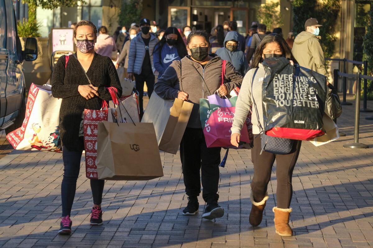 FILE - Black Friday shoppers wearing face masks carry bags at the Citadel Outlets in Commerce, Calif., Friday, Nov. 26, 2021. The National Retail Federation, the nation’s largest retail trade group, expects that holiday sales growth this year will slow to a range of 6% to 8%, compared to 13.5% a year ago. The trade group said Thursday, Nov. 3, 2022, that it predicts that sales for the November and December period will grow to between $942.6 billion to $960.4 billion. (AP Photo/Ringo H.W. Chiu, File)