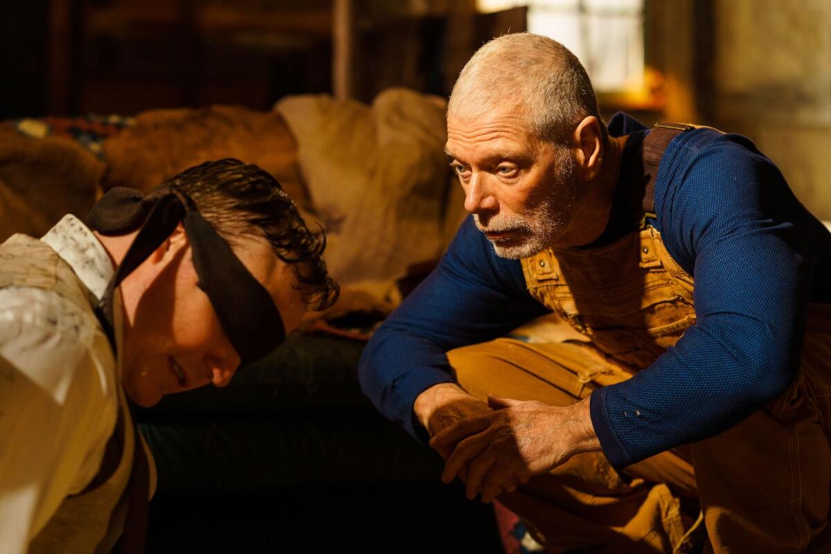 A man in overalls squats beside a blindfolded man in the movie "Old Man."