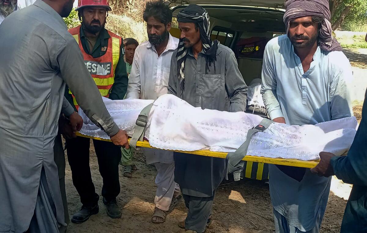 A rescue worker and villagers carry the body of a victim of a boat accident on the Indus River, in Sadiqabad district, about 350 kilometers (210 miles) south of Multan, Pakistan, Monday, July 18, 2022. The passenger boat carrying nearly 100 members of a wedding party capsized on Monday in the fast-flowing Indus River in eastern Punjab province, killing more than a dozen people, government and rescue officials said. (AP Photo/Mohammad Shabaan)