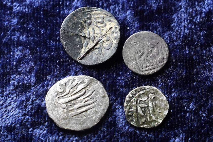Cuatro monedas de plata del siglo XVII con inscripciones en árabe yacen sobre una mesa el jueves 27 de octubre de 2022, en Warwick, Rhode Island. La moneda ubicada arriba a la izquierda fue hallada en Connecticut, mientras que las otras tres fueron encontradas en Rhode Island. (AP Foto/Steven Senne)