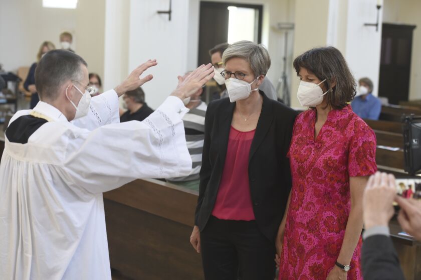 Vicar Wolfgang Rothe, left, blesses the couple Christine Walter, center, and Almut Muenster, right, during a Catholic service with the blessing of same-sex couples in St Benedict's Church in Munich, Sunday, May 9, 2021. Germany’s Catholic progressives are openly defying a recent Holy See pronouncement that priests cannot bless same-sex unions by offering exactly such blessings at services in about 100 different churches all over the country. The blessings at open worship services are the latest pushback from German Catholics against a document released in March by the Vatican’s orthodoxy office, which said Catholic clergy cannot bless same-sex unions. (Felix Hoerhager/dpa via AP)