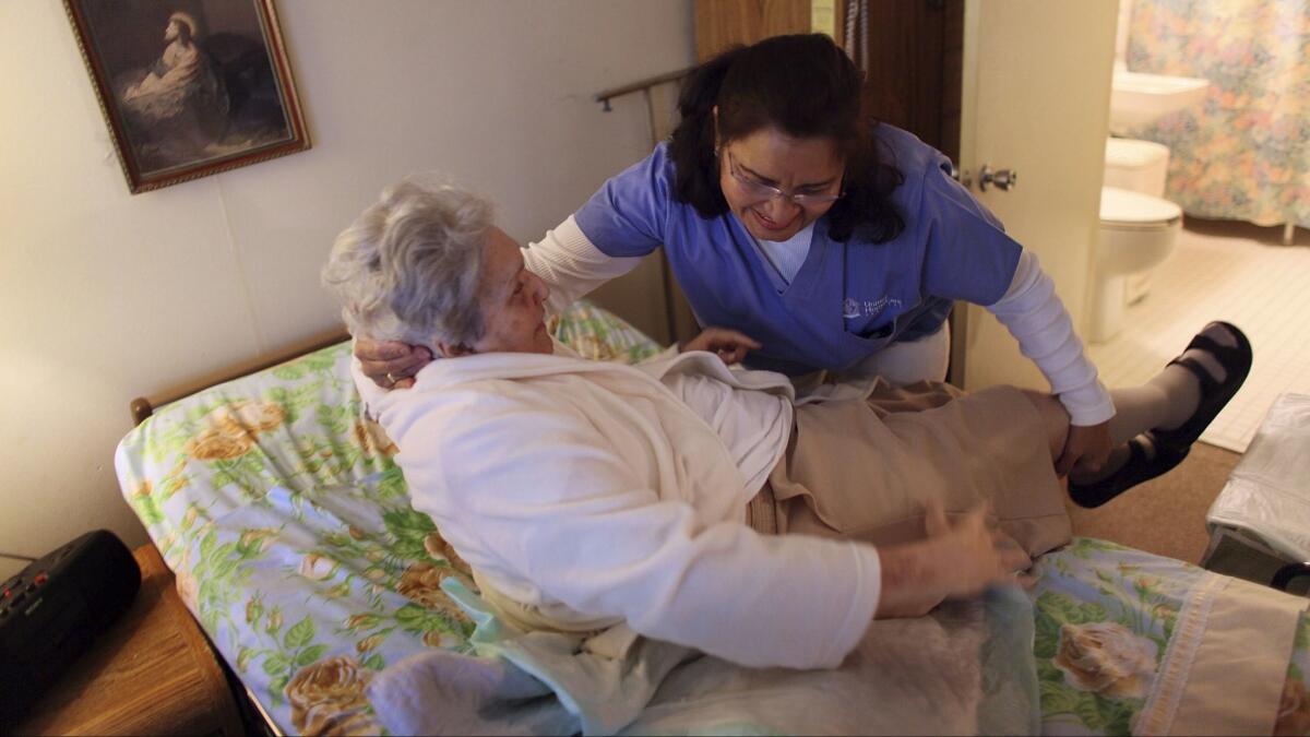 A home health aide helps a woman get out of bed.