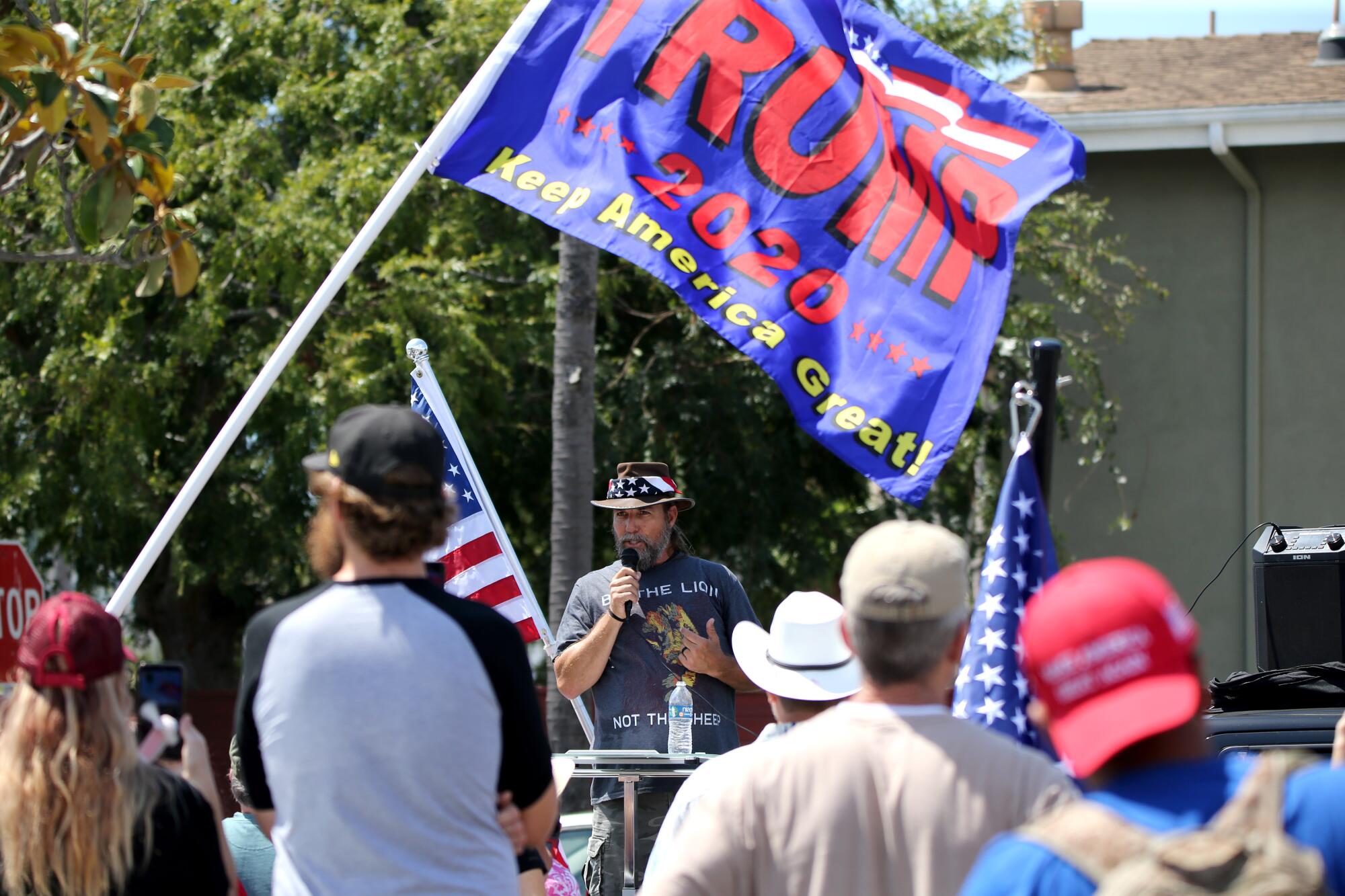 Alan Hostetter speaks protesters waving U.S. flags and a large Trump 2020: Make America Great Again flag