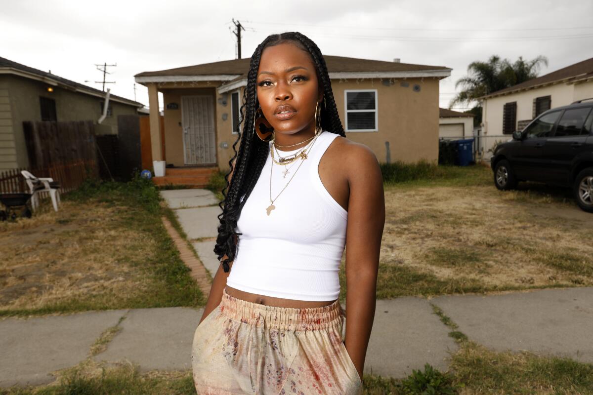 A woman stands in front of the sidewalk in front of a house.