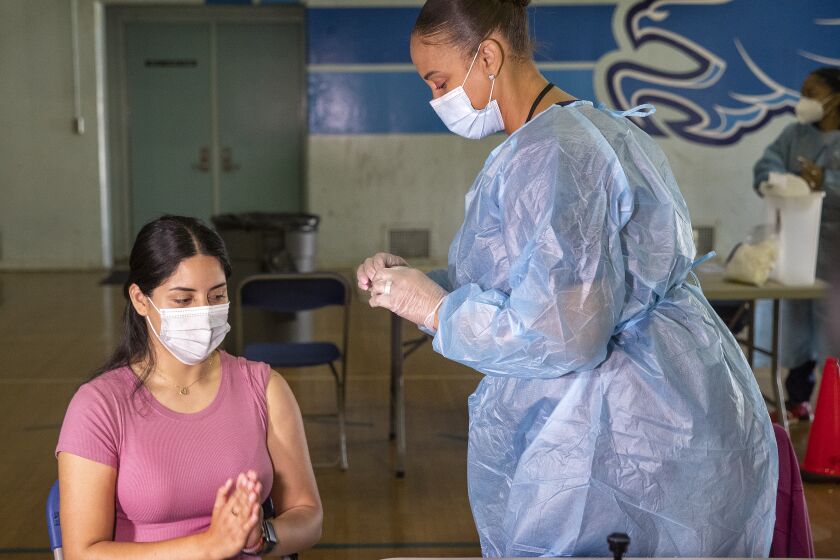 SAN FERNANDO, CA - AUGUST 30, 2021: Angela Saveva, 21, a teacher's assistant at San Fernando Middle School in San Fernando, is thankful after receiving the first dose of the Pfizer vaccine from Tracy Jones, a licensed vocational nurse. A mobile COVID-19 vaccine clinic was set up inside the gymnasium at San Fernando Middle School to inoculate LAUSD employees and students age 12 and older. (Mel Melcon / Los Angeles Times)