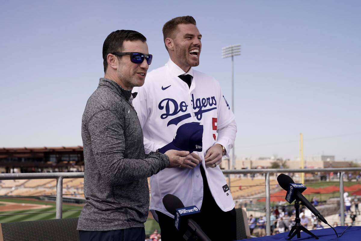 Andrew Friedman stands next to Freddie Freeman, who buttons on a Dodgers uniform.