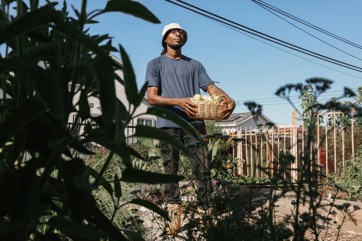 A man holds a bowl of fruit while standing in the middle of a garden 