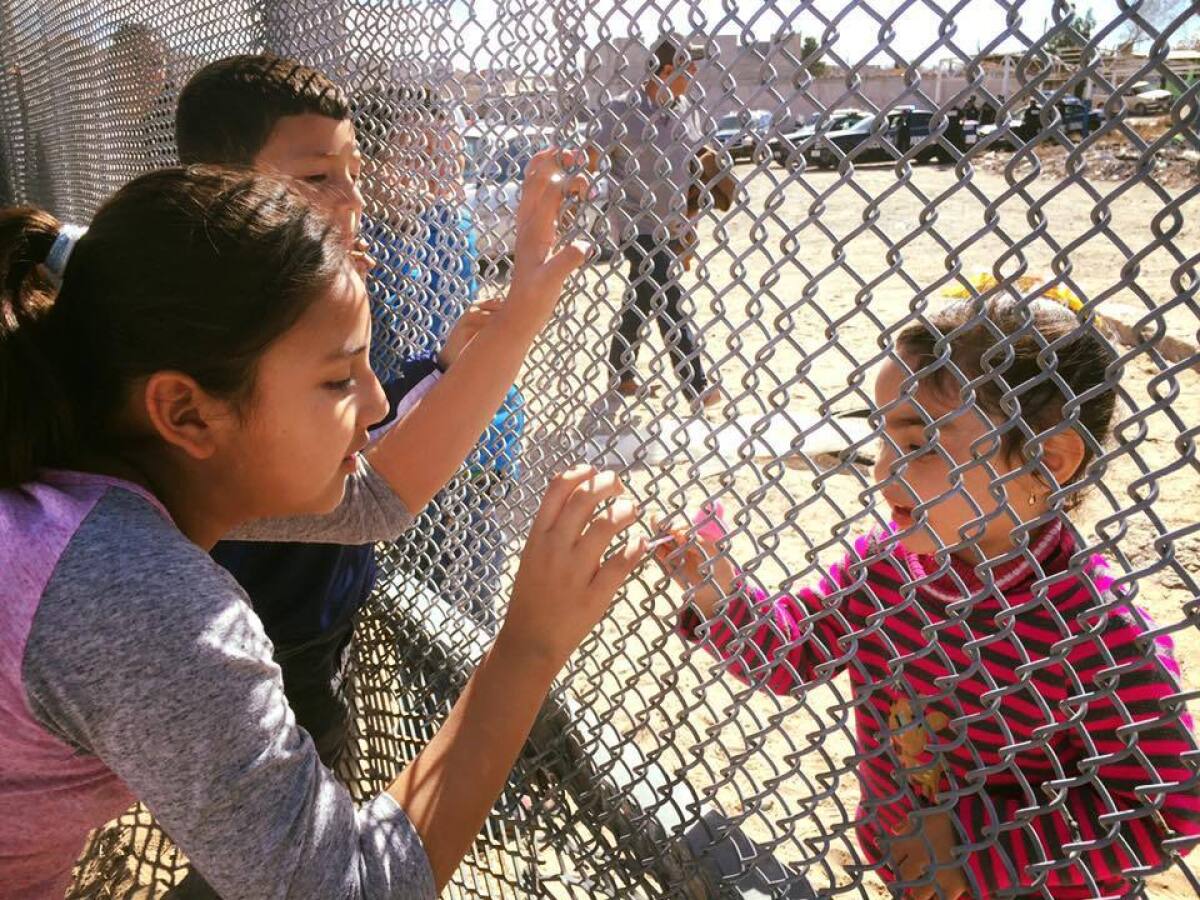 Cousins swap candy through the border fence.