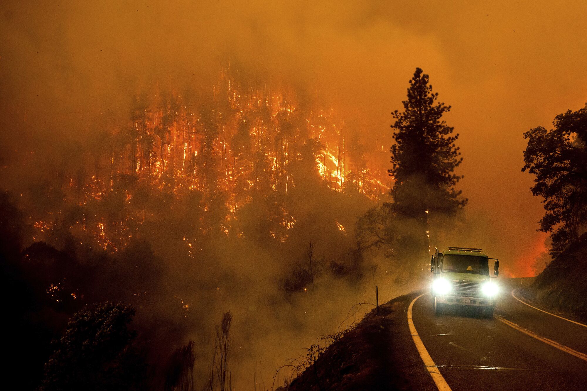 A firetruck on a highway with a forest burning in the background